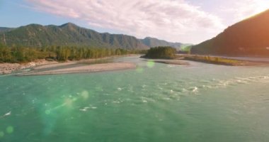 4k UHD hava görüntüsü. Güneşli yaz sabahında taze soğuk dağ nehri üzerinde alçak uçuş. Horisont 'ta yeşil ağaçlar ve güneş ışınları