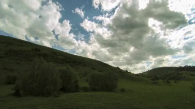 Yazın 4K UHD dağ çayırı zaman dilimi. Bulutlar, ağaçlar, yeşil çimenler ve güneş ışınları hareketi.
