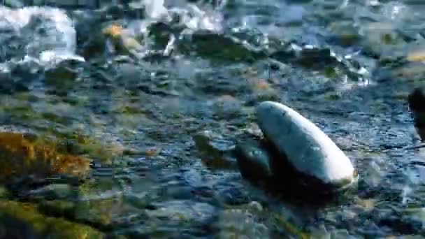 Dolly deslizante tiro da água espirrando em um rio de montanha perto da floresta. Rochas molhadas e raios solares. Movimento horizontal estável. — Vídeo de Stock