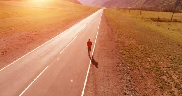 Voo de baixa altitude na frente do homem desportivo na estrada de asfalto perfeito — Vídeo de Stock