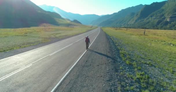 アスファルトの道路を歩くヒッチハイカーの観光客の上のフライト。夏の日に巨大な田舎の谷。リュックハイキング男. — ストック動画