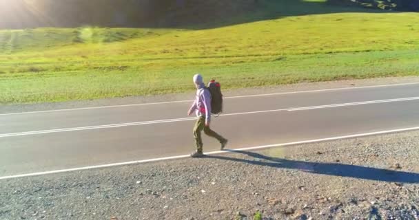 Flyg över liftare turist promenader på asfalterad väg. Enorm lantlig dal på sommardagen. Ryggsäck vandring kille. — Stockvideo