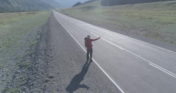 Zbor peste autostopist turist de mers pe jos pe drum asfalt. Vale rurală imensă în ziua de vară. Rucsac drumeții tip . — Videoclip de stoc