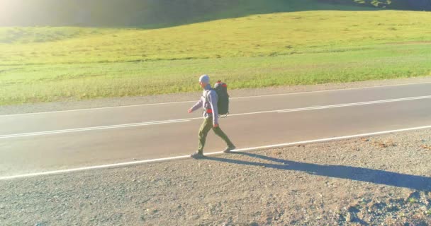 Volo sopra autostoppista turistico a piedi su strada asfaltata. Enorme valle rurale durante la giornata estiva. Zaino escursionista ragazzo. — Video Stock