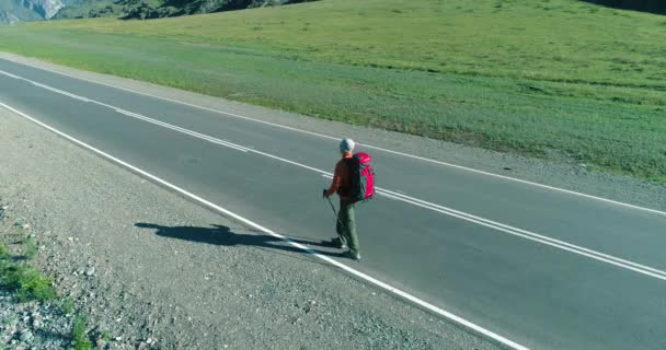 Flight over hitchhiker tourist walking on asphalt road. Huge rural valley at summer day. Backpack hiking guy. — Stock Video