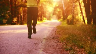 Asfalt yolda koşan sporcu. Kırsal şehir parkı. Yeşil ağaç ormanı ve ufukta güneş ışığı.