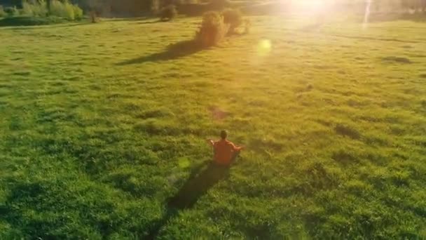 完璧な緑の芝生でスポーツヨガの男の上に低高度放射線飛行。山の夕日. — ストック動画