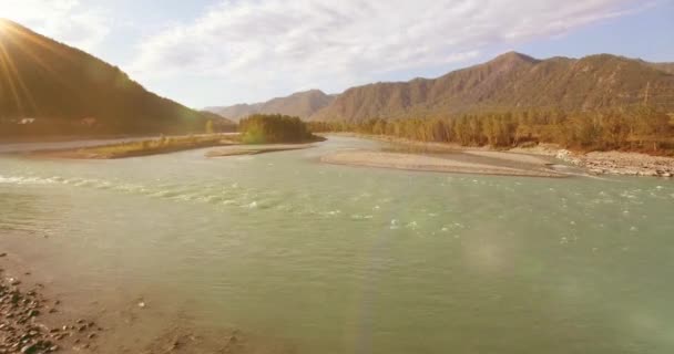 Vol à basse altitude au-dessus d'une rivière de montagne fraîche et rapide avec des rochers au soleil matin d'été. — Video