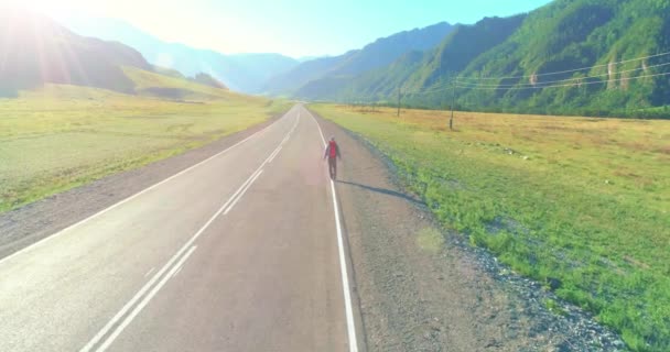 Flight over hitchhiker tourist walking on asphalt road. Huge rural valley at summer day. Backpack hiking guy. — Stock Video