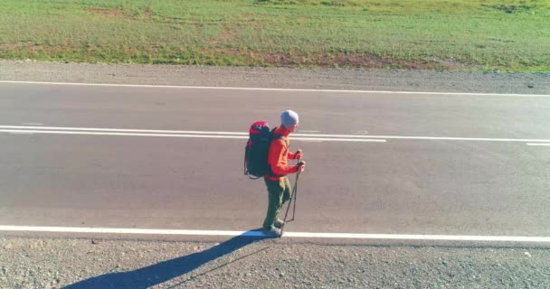 アスファルトの道路を歩くヒッチハイカーの観光客の上のフライト。夏の日に巨大な田舎の谷。リュックハイキング男. — ストック動画