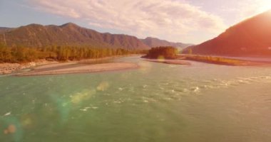 4k UHD hava görüntüsü. Güneşli yaz sabahında taze soğuk dağ nehri üzerinde alçak uçuş. Horisont 'ta yeşil ağaçlar ve güneş ışınları