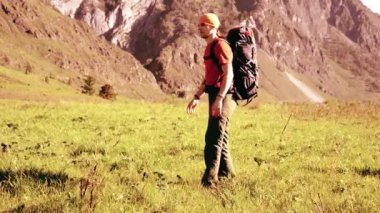 Sırt çantası ile yeşil dağ çayır üzerinde yürüyen adam hiking. Yaz spor ve eğlence kavramı.