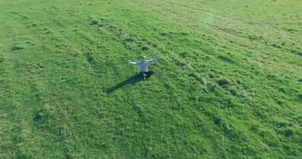 Vol orbital bas autour de l'homme sur herbe verte avec bloc-notes au champ rural jaune. — Video