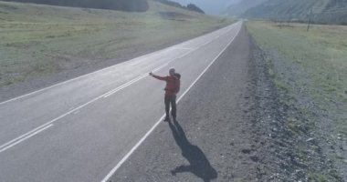 Asfalt yolda yürüyen otostopçu turist üzerinden uçuş. Yaz günü büyük bir kırsal vadi. Sırt çantalı gezgin..