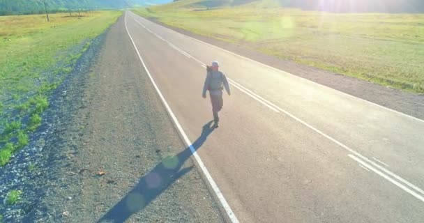 Repülés egy stoppos turista felett, aki aszfalt úton sétál. Hatalmas vidéki völgy a nyári napokon. Hátizsákos túrázó.. — Stock videók