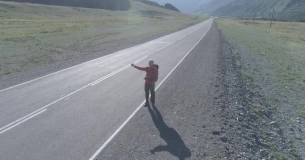 Zbor peste autostopist turist de mers pe jos pe drum asfalt. Vale rurală imensă în ziua de vară. Rucsac drumeții tip . — Videoclip de stoc