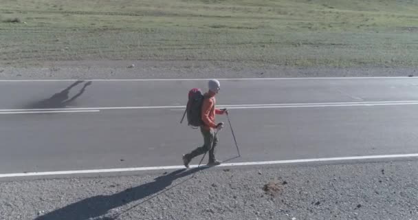 Flight over hitchhiker tourist walking on asphalt road. Huge rural valley at summer day. Backpack hiking guy. — Stock Video