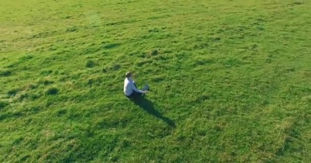 Vuelo orbital bajo alrededor del hombre sobre hierba verde con bloc de notas en el campo rural amarillo. — Vídeos de Stock