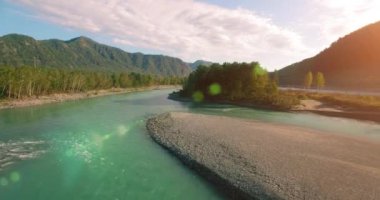 4k UHD hava görüntüsü. Güneşli yaz sabahında taze soğuk dağ nehri üzerinde alçak uçuş. Horisont 'ta yeşil ağaçlar ve güneş ışınları