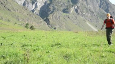 Sırt çantası ile yeşil dağ çayır üzerinde yürüyen adam hiking. Yaz spor ve eğlence kavramı.