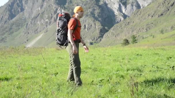 ハイキングのバックパックと緑山の牧草地の上を歩く男。夏のスポーツとレクリエーションの概念. — ストック動画