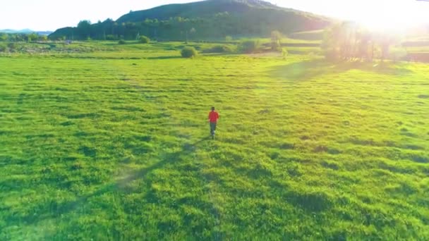 完璧な緑の芝生の牧草地でスポーツマンの上を飛行します。山の夕日 — ストック動画