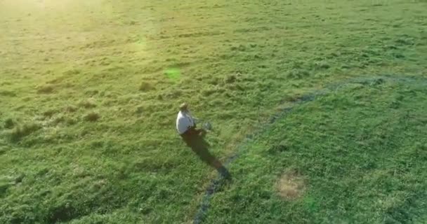 Vuelo orbital bajo alrededor del hombre sobre hierba verde con bloc de notas en el campo rural amarillo. — Vídeos de Stock