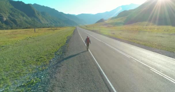 アスファルトの道路を歩くヒッチハイカーの観光客の上のフライト。夏の日に巨大な田舎の谷。リュックハイキング男. — ストック動画