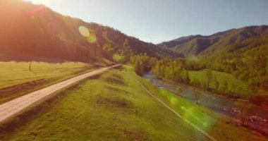 Güneşli yaz sabahında taze dağ nehri ve çayır üzerinde uçuşun ortasında. Aşağıdaki kırsal toprak yol.
