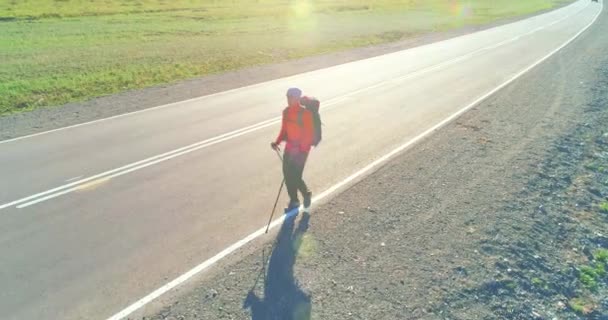 アスファルトの道路を歩くヒッチハイカーの観光客の上のフライト。夏の日に巨大な田舎の谷。リュックハイキング男. — ストック動画