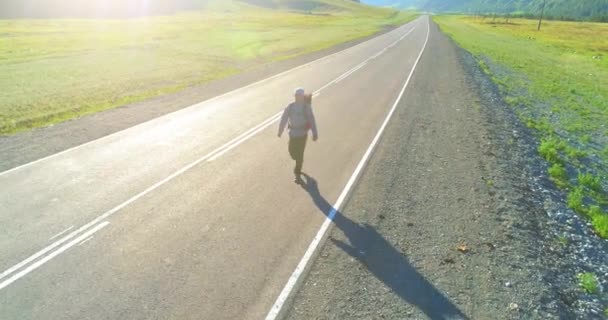 Volo sopra autostoppista turistico a piedi su strada asfaltata. Enorme valle rurale durante la giornata estiva. Zaino escursionista ragazzo. — Video Stock