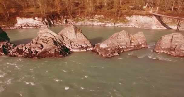 Vol à basse altitude au-dessus d'une rivière de montagne fraîche et rapide avec des rochers au soleil matin d'été. — Video