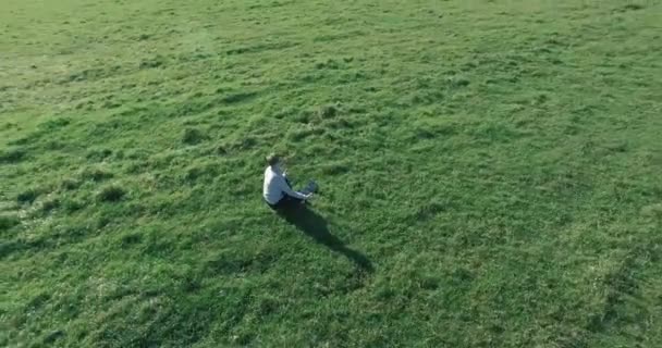 Низький орбітальний політ навколо людини на зеленій траві з блокнотом на жовтому сільському полі . — стокове відео