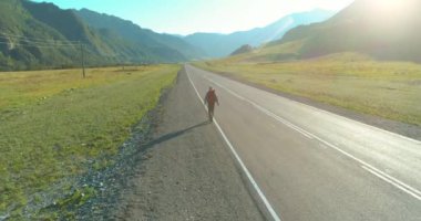 Asfalt yolda yürüyen otostopçu turist üzerinden uçuş. Yaz günü büyük bir kırsal vadi. Sırt çantalı gezgin..