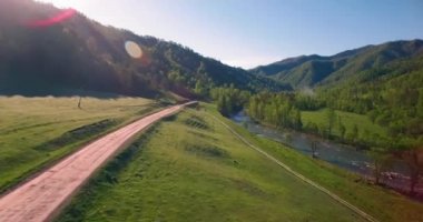 Güneşli yaz sabahında taze dağ nehri ve çayır üzerinde uçuşun ortasında. Aşağıdaki kırsal toprak yol.