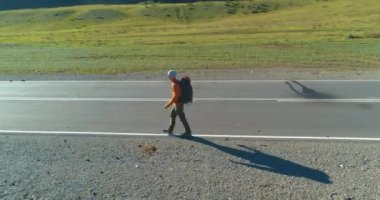 Asfalt yolda yürüyen otostopçu turist üzerinden uçuş. Yaz günü büyük bir kırsal vadi. Sırt çantalı gezgin..