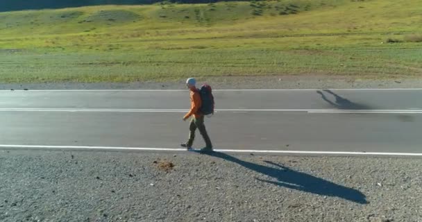 Voo sobre carona turista andando na estrada de asfalto. Vale rural enorme no dia de verão. Mochila caminhadas cara. — Vídeo de Stock