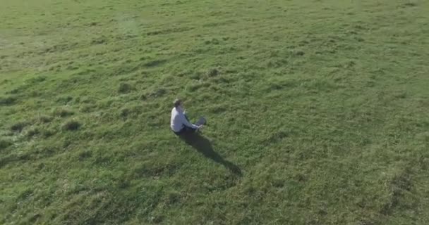 Low orbital flight around man on green grass with notebook pad at yellow rural field. — Stock Video