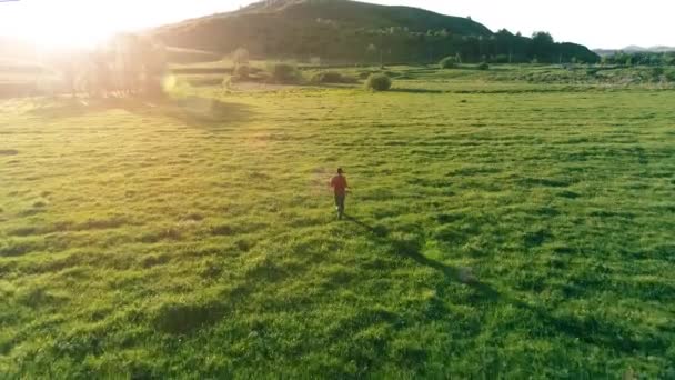 Vuelo sobre el hombre del deporte en el prado de hierba verde perfecto. Puesta de sol en montaña — Vídeos de Stock