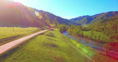 Güneşli yaz sabahında taze dağ nehri ve çayır üzerinde uçuşun ortasında. Aşağıdaki kırsal toprak yol.