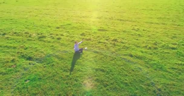 Vol orbital bas autour de l'homme sur herbe verte avec bloc-notes au champ rural jaune. — Video