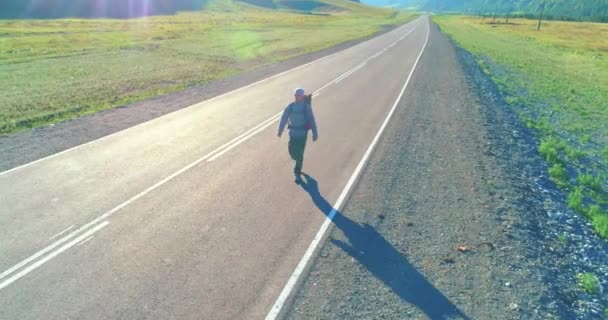 Flight over hitchhiker tourist walking on asphalt road. Huge rural valley at summer day. Backpack hiking guy. — Stock Video