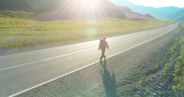 Asfalt yolda yürüyen otostopçu turist üzerinden uçuş. Yaz günü büyük bir kırsal vadi. Sırt çantalı gezgin..