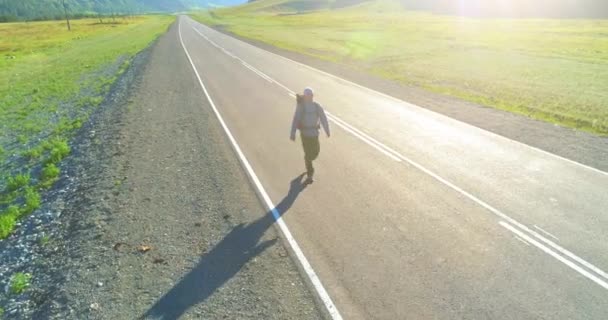 Flight over hitchhiker tourist walking on asphalt road. Huge rural valley at summer day. Backpack hiking guy. — Stock Video