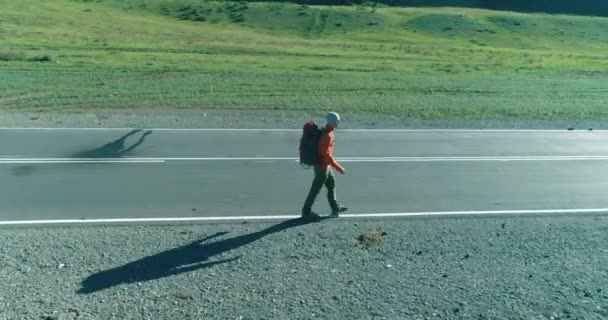 Volo sopra autostoppista turistico a piedi su strada asfaltata. Enorme valle rurale durante la giornata estiva. Zaino escursionista ragazzo. — Video Stock