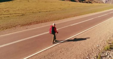 Asfalt yolda yürüyen otostopçu turist üzerinden uçuş. Yaz günü büyük bir kırsal vadi. Sırt çantalı gezgin..