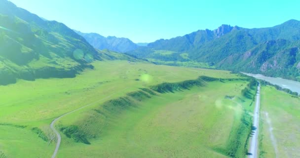 Aerial rural mountain road and meadow at sunny summer morning. Asphalt highway and river. — Stock Video