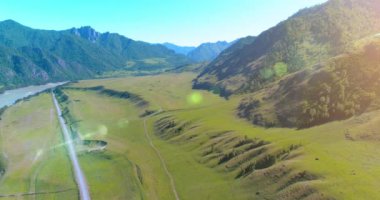 Güneşli yaz sabahında havadan kırsal dağ yolu ve çayır. Asfalt karayolu ve nehir.