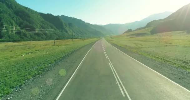 Voo aéreo de baixo ar sobre a estrada da montanha e o prado na ensolarada manhã de verão . — Vídeo de Stock