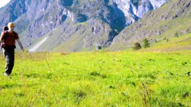 Sırt çantası ile yeşil dağ çayır üzerinde yürüyen adam hiking. Yaz spor ve eğlence kavramı.